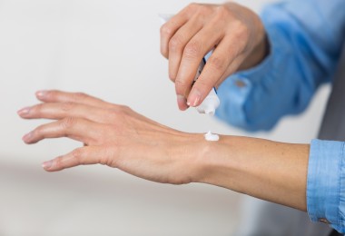 Die Nahaufnahme zeigt eine Person, die aus einer Tube eine kleine Menge weißer Creme auf den Handrücken aufträgt.