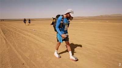 Protagonist geht mit einem Rucksack in einer Wüste. Deutlich hinter ihm sind zwei weitere Läufer.